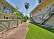 Thumbnail 6 of 17 - A long, narrow walkway with a grassy area on one side and a building on the other.