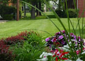 Thumbnail 12 of 16 - A flower bed with red and white flowers in front of a building.