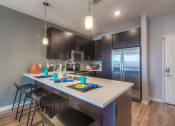 Thumbnail 74 of 78 - a kitchen with a large island with a sink and three stools  at EdgeWater at City Center, Lenexa