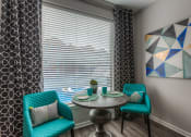 Thumbnail 61 of 78 - a small dining table with two blue chairs and a large window with blinds  at EdgeWater at City Center, Lenexa, KS