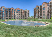 Thumbnail 21 of 78 - a fountain in the middle of a grassy area with an apartment complex in the background  at EdgeWater at City Center, Lenexa, 66219