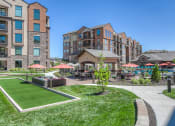Thumbnail 20 of 78 - a grassy area with umbrellas and tables and chairs in front of an apartment building at EdgeWater at City Center, Lenexa, Kansas
