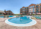 Thumbnail 13 of 78 - a swimming pool with lounge chairs and umbrellas with a resort style building in the background at EdgeWater at City Center, Lenexa