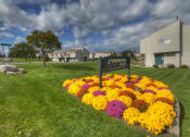 Thumbnail 13 of 22 - Front Sign with Flowers and Green Lawn at Stone Hedge Village Townhouses, Farmington, NY