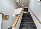 Thumbnail 10 of 21 - A staircase with a wooden handrail and a grey carpeted runner.