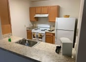 Thumbnail 16 of 17 - A kitchen fully equipped with appliances, including a white fridge, white stove, and brown cabinets.