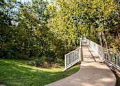 Thumbnail 31 of 40 - Curved walking path leading to pedestrian bridge at The Brook At Columbia Apartments, Columbia, Maryland