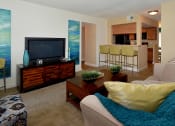 Thumbnail 3 of 13 - a living room with a television and a kitchen in the background at Broadwater Apartments in St Petersburg, FL 33711