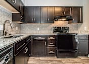 Thumbnail 7 of 28 - Kitchen with dark wood cabinets and stainless appliances at Verano Oaks Apartments