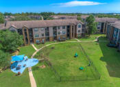 Thumbnail 22 of 44 - Dog-Friendly Apartments in Spring, TX - Overhead View of Fenced off Dog Park with Seperate Covered Seating Area Surrounded by Lush Greenery.