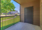 Thumbnail 21 of 44 - Pet-Friendly Apartments in Spring, TX - Spacious Patio with Metal Railing, a Storage Room and a View of Grass and Trees.