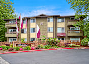 Thumbnail 1 of 19 - Exterior view of manicured grounds and building, and blue skies in the background at Heritage Grove, Renton, WA.