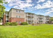 Thumbnail 12 of 15 - exterior of Creekside at Tasker's Chance in Frederick, MD with grass on either side of walkway to building and shrubs around building exterior