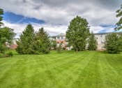 Thumbnail 11 of 15 - exterior of Creekside at Taskers Chance with grass, trees in back near building and blue sky with clouds