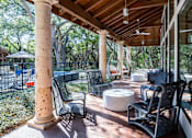 Thumbnail 43 of 48 - Covered outdoor terrace with wicker seating and pool views at Nalle Woods of Westlake Apartments, Austin, 78746
