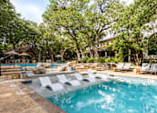 Thumbnail 13 of 48 - Pool area with tanning ledge and stone features at Nalle Woods of Westlake Apartments, Austin, Texas