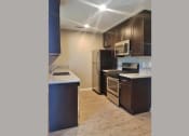 Thumbnail 2 of 33 - Angled view of kitchen area with brown cabinets, stone counters, stainless appliances and wood look flooring