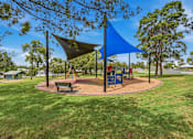 Thumbnail 16 of 20 - A playground with a blue shade structure and a green bench.