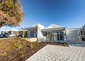Thumbnail 7 of 11 - A modern white house with a grey roof and a driveway in front.