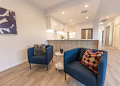 Thumbnail 2 of 11 - A living room with a blue couch and a painting on the wall.
