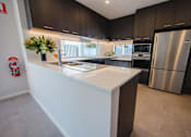 Thumbnail 4 of 9 - A modern kitchen with dark brown cabinets and a white island.