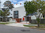 Thumbnail 1 of 6 - A modern building with a white facade and a black fence in front.