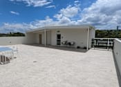 Thumbnail 4 of 6 - A white building with a table and chairs outside.