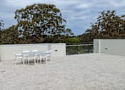 Thumbnail 3 of 6 - A patio with a table and chairs is surrounded by trees.