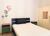 Thumbnail 3 of 12 - a small bedroom with a bed and a pink flower on the wall