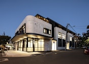 Thumbnail 1 of 14 - a white building with windows and a street at night