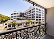 Thumbnail 1 of 14 - A balcony with a black railing overlooks a large building with many windows.