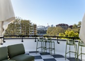 Thumbnail 1 of 15 - A balcony with a green couch and chairs overlooking a city skyline.