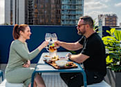 Thumbnail 26 of 34 - a man and a woman sitting at a table on a balcony drinking wine and eating