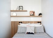 Thumbnail 3 of 14 - a bedroom with a bed with white pillows and a wooden shelf above it