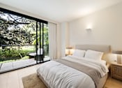 Thumbnail 13 of 24 - A bedroom with a large bed and a view of the outdoors through a glass door.