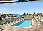 Thumbnail 8 of 24 - A swimming pool on a wooden deck with a cityscape in the background.