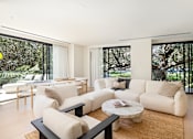 Thumbnail 12 of 24 - A living room with white furniture and a large window.