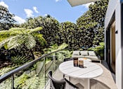 Thumbnail 1 of 24 - A balcony with a table and chairs overlooks a lush green garden.