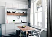 Thumbnail 1 of 12 - a small kitchen with white cabinets and a wooden table