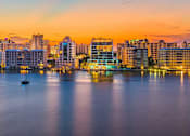 Thumbnail 3 of 6 - A city skyline at dusk with buildings reflecting on the water.