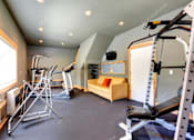 Thumbnail 7 of 9 - A well-equipped home gym with a bench, weights, and cardio equipment.