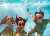Thumbnail 21 of 32 - Three women are swimming underwater in a pool.