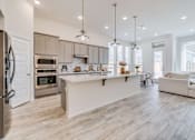 Thumbnail 6 of 10 - A modern kitchen with a refrigerator on the left and a dining area with a white couch.