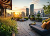 Thumbnail 5 of 7 - A rooftop patio with a couch, pillows, and plants overlooking a city skyline at sunset.