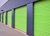 Thumbnail 2 of 9 - A series of green storage units with grey pillars and a grey roof.