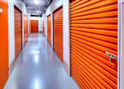 Thumbnail 5 of 9 - A long hallway with orange doors in a storage facility.
