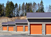Thumbnail 1 of 5 - a row of garages with orange doors and trees in the background