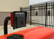Thumbnail 3 of 9 - A red car is parked next to a black gate with a parking meter attached to it.