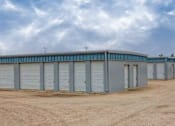Thumbnail 5 of 9 - A large grey building with multiple roll-up doors is situated in a barren landscape.