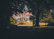 Thumbnail 3 of 5 - A large house is seen through the trees in the distance.